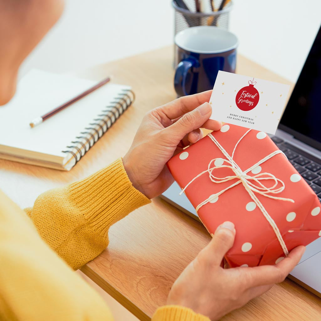 A person in a corporate office holding a wrapped gift box of brownies and a note that says Merry Christmas and Happy New Year